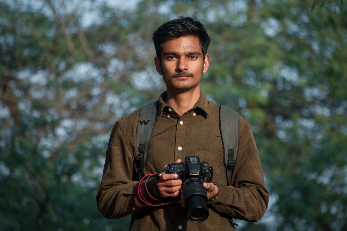 Een jonge man houdt een DSLR-camera vast in een buitensetting, klaar voor de fotografie.